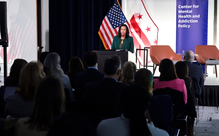 A woman standing on stage speaks to crowd.