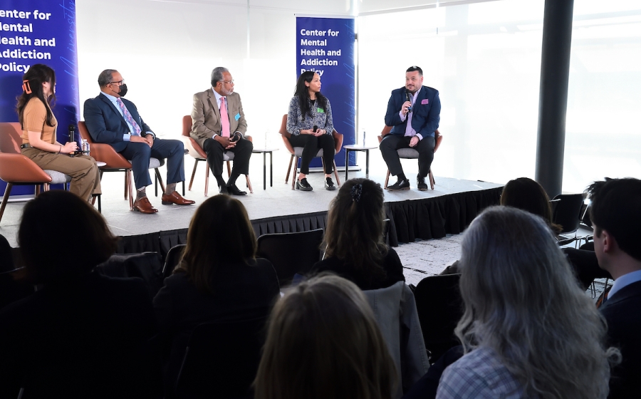 Five adults seated on venue stage with microphone in hand.