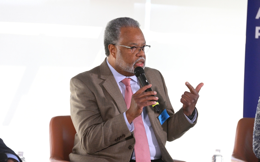 A man seated on stage speaks into a microphone.