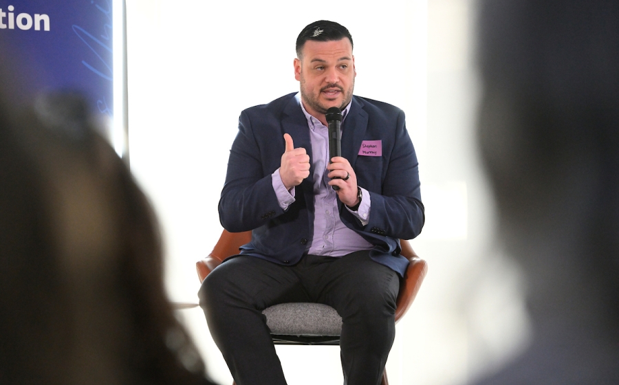 A man seated on stage speaks into a microphone.