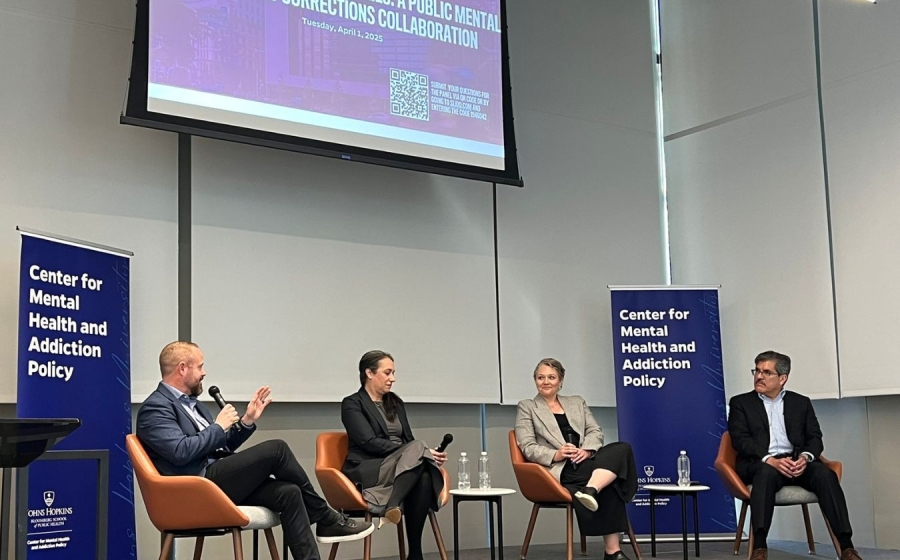 Four adults wearing business casual attire sit on stage.