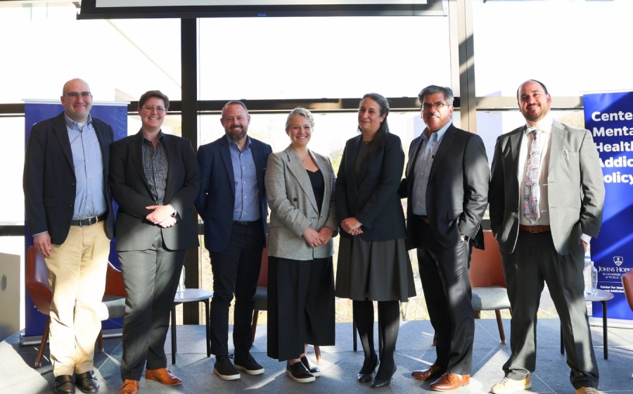 Seven adults wearing business attire stand side by side on stage.