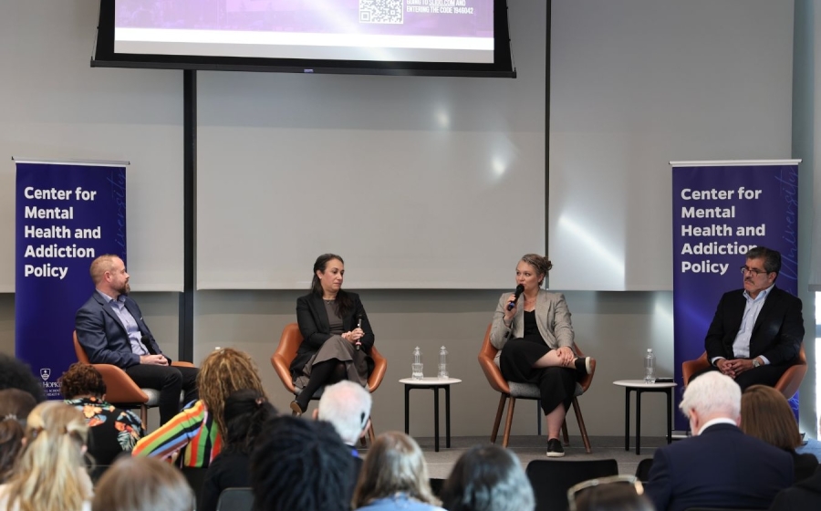 Four adults wearing business casual attire sit on stage.