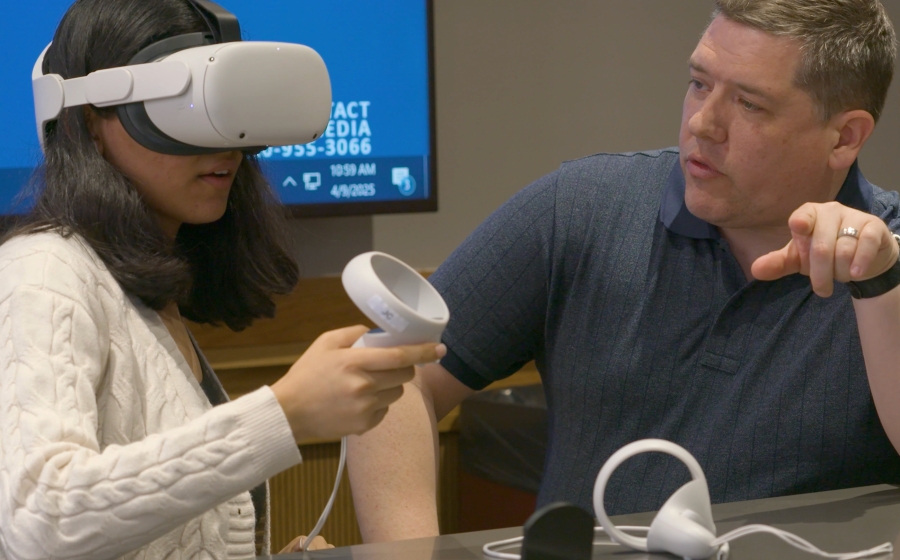 Woman wearing a VR simulator headset and man sitting next to her pointing