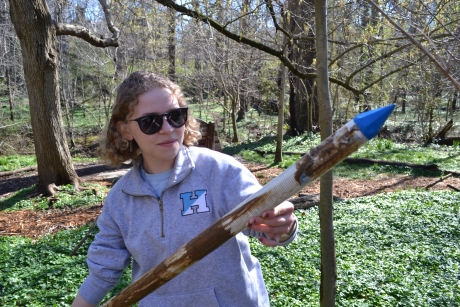 A young female holds a pointed pole with a wooded background
