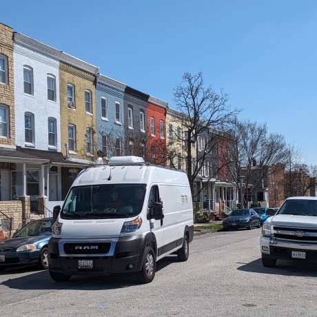 EHE-Mobile-Air-Lab White van parked in front of multi-colored rowhouses