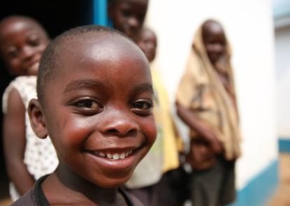 A young boy smiling in a sunny alley, behind him are three other people watching on