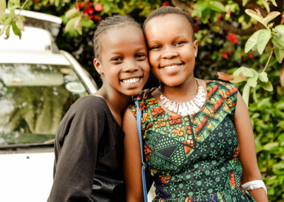 Two Kenyan adolescent girls, standing outside smiling