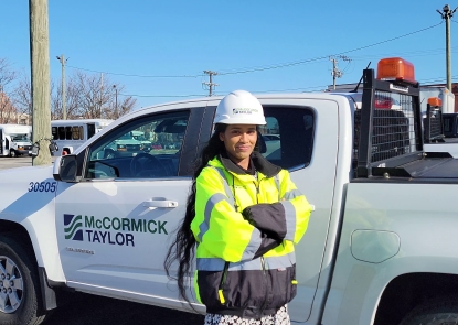 Woman in a hard hat and yellow vest standing in front of a white business truck