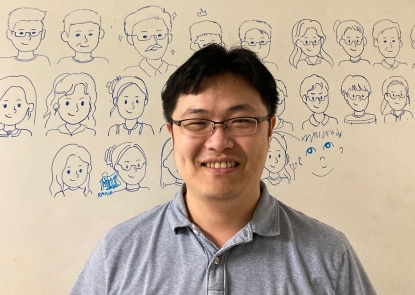 YuNing Lu stands in front of a whiteboard with cartoons of lab members drawn on it