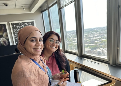 Two Bloomberg School PRFH students smile near a skyline view of Baltimore in the 9th floor cafe.